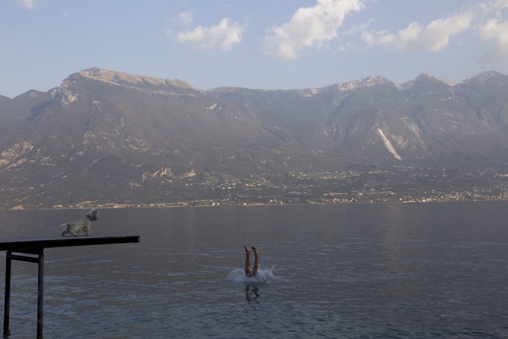 Sprung ins Wasser vom Steg, dahinter die Berge am Gardasee