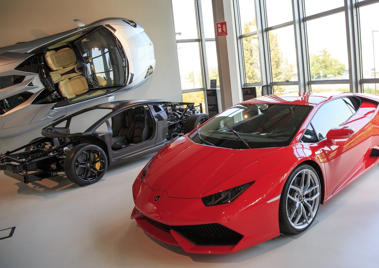 Roter Lamborghini Huracán im Museum, dahinter ein Chassis-Schnittmodell und eine Karosserie an der Wand