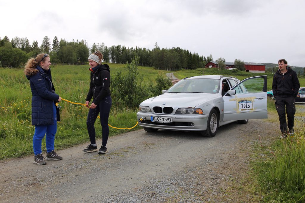 Zwei Frauen ziehen das Rallye-Fahrzeug an einem gelben Abschleppseil über eine Schotterstraße